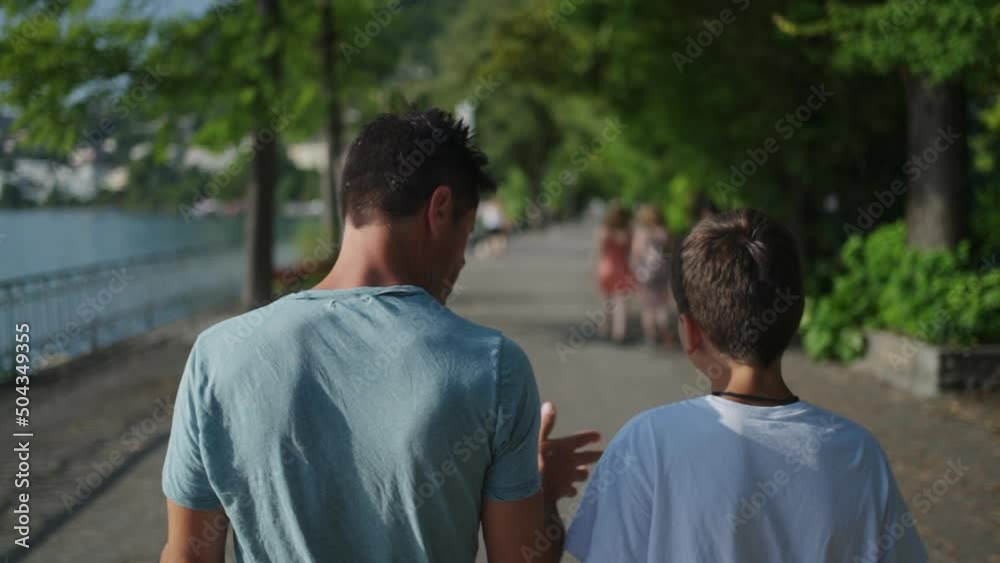 Back of father giving advice to son walking outside by lake Back of father giving advice to son walking outside by lake