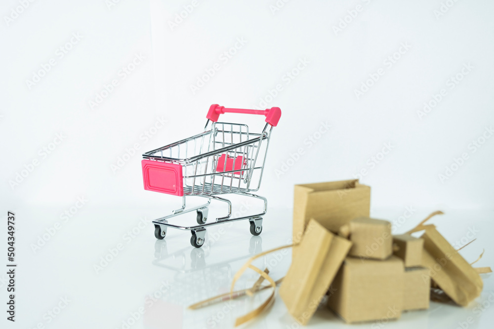 Mini supermarket handcart and cardboard box isolated on white background, copy space, selective focus, online marketing and shopping concept, carton box and pink metal market cart, miniature object