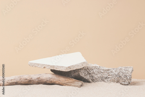 Grunge concrete stones and dry tree twigs on white beach sand background. Minimal creative composition background for cosmetics or products presentation. Front view