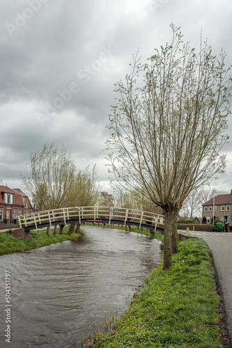Small footbridge over the narrow Dutch peat river Noordeloos in the village of Noordeloos, municipality of Molenlanden, Alblasserwaard region, province of South Holland. It is a cloudy day in spring. photo