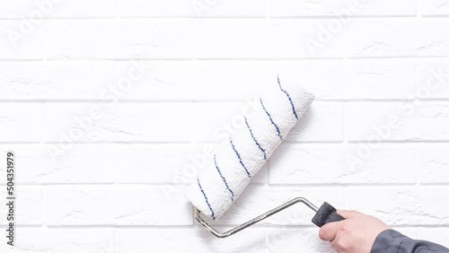 A man's hand with a roller paints the wall with white paint. Painting a white brick wall