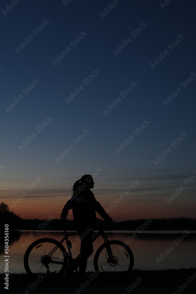 Obraz premium Silhouette of woman with mountain bike on colorful blue sky sunset background. Active outdoors lifestyle