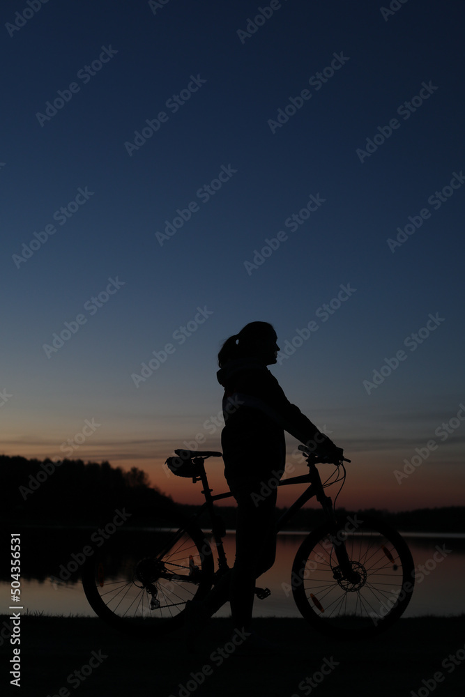 Obraz premium Silhouette of woman with mountain bike on colorful blue sky sunset background. Active outdoors lifestyle