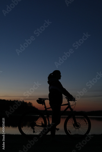 Silhouette of woman with mountain bike on colorful blue sky sunset background. Active outdoors lifestyle