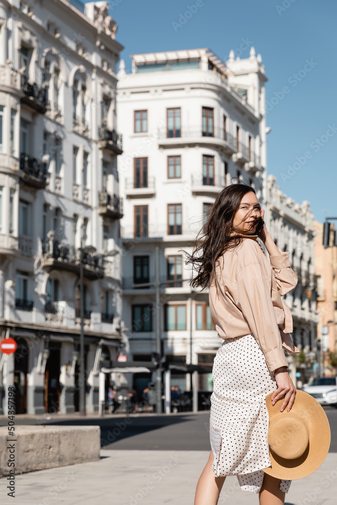 brunette woman with straw hat looking at camera on street.