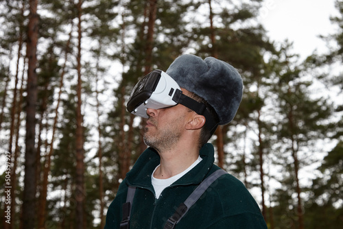 Mushroom picker and virtual reality. A man wearing virtual reality glasses in the forest near a campfire.
