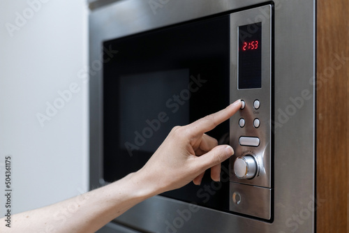 Person's hand pressing microwave oven button to start defrosting food