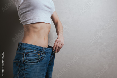 young woman dressed in wide jeans and a white shirt, demonstrates successful weight loss. concept of diet and weight loss