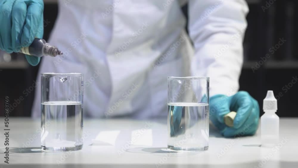 A male chemist in the laboratory drips a red liquid into glass cones with water A male chemist in the laboratory drips a red liquid into glass cones with water
