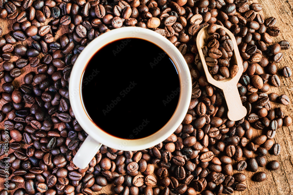 Fototapeta premium Black coffee in the cup, Dark Coffee beans on the old wooden floor, Close up of seeds of coffee.