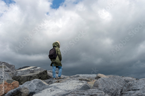 Backpacker at top of a rocky mountain pass with a stormy sky and high winds.