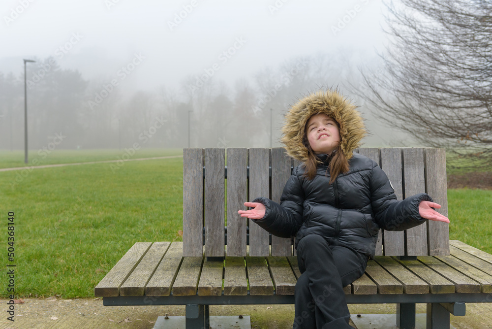 Fototapeta premium Enjoying a winter walk in the park. Teenage girl on a bench in cold weather in a warm jacket