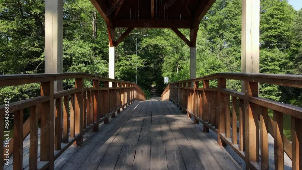 low angle aerial view tilting up from old ancient bridge revealing green forest in background. Wooden bridge river in sunny day. low angle aerial view tilting up from old ancient bridge revealing green forest in background. Wooden bridge river in sunny day.