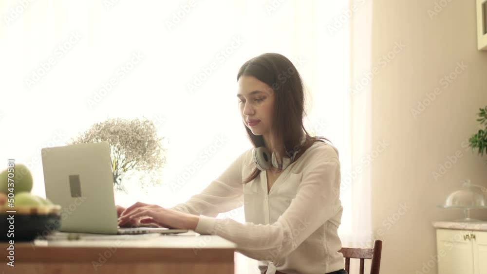 Portrait of attractive woman using laptop in modern domestic kitchen. Young woman sitting in front open laptop computer. Study, learning, remote work, freelance.