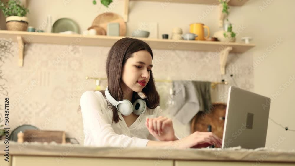 Portrait of attractive woman using laptop in modern domestic kitchen. Young woman sitting in front open laptop computer. Study, learning, remote work, freelance. Portrait of attractive woman using laptop in modern domestic kitchen. Young woman sitting in front open laptop computer. Study, learning, remote work, freelance.