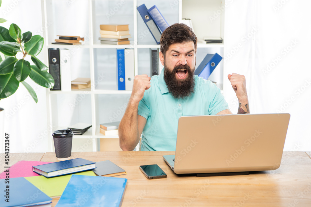 Excited businessman celebrating victory looking in laptop at office desk, business success Excited businessman celebrating victory looking in laptop at office desk, business success