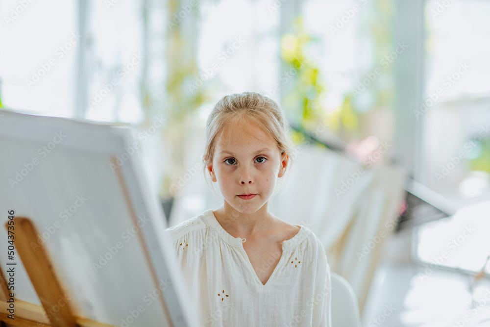 Young girl in white shirt and jeans painting big picture stands on the easel Young girl in white shirt and jeans painting big picture stands on the easel