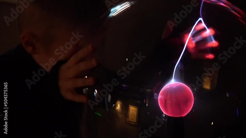 A child makes experiments on an electric plasma ball. photo