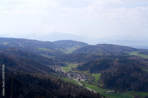 Panoramic view from local mountain Uetliberg with valley, village, agricultural fields and Swiss Alps in the background on a blue cloudy spring day. Photo taken April 14th, 2022, Zurich, Switzerland. © Michael Derrer Fuchs