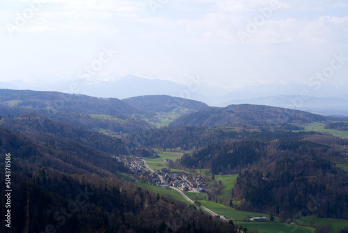 Panoramic view from local mountain Uetliberg with valley, village, agricultural fields and Swiss Alps in the background on a blue cloudy spring day. Photo taken April 14th, 2022, Zurich, Switzerland.