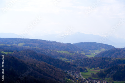 Panoramic view from local mountain Uetliberg with valley, village, agricultural fields and Swiss Alps in the background on a blue cloudy spring day. Photo taken April 14th, 2022, Zurich, Switzerland. © Michael Derrer Fuchs