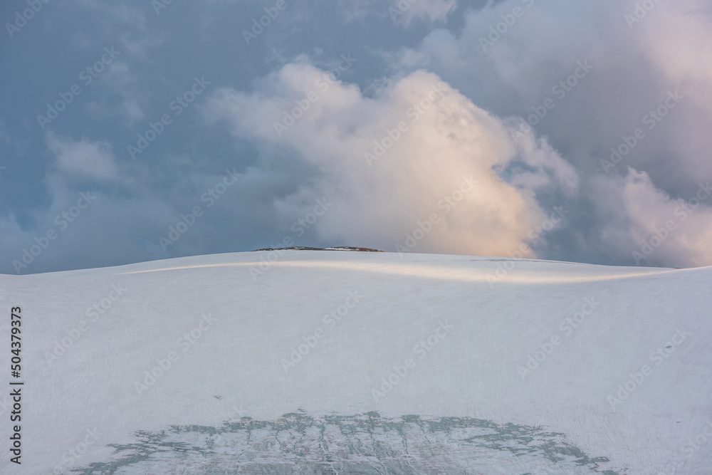 Dramatic landscape with glacier on sunlit high snow mountain top under cloudy sky at sunset. Beautiful alpine landscape with large snowy mountain in sunlight under evening clouds at changeable weather Dramatic landscape with glacier on sunlit high snow mountain top under cloudy sky at sunset. Beautiful alpine landscape with large snowy mountain in sunlight under evening clouds at changeable weather