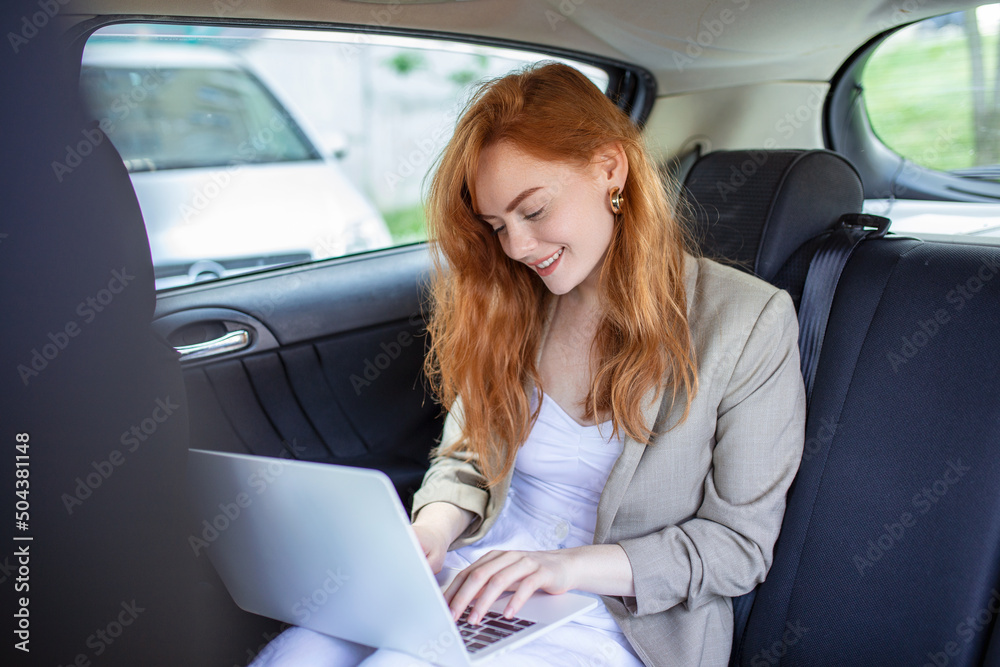Pensive businesswoman with laptop in back seat of car. Young woman using a laptop in a car.