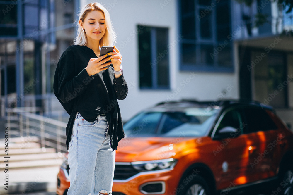 Fototapeta premium Woman using phone in the street by the car