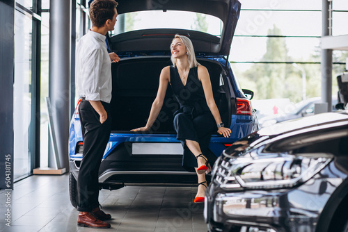 Young couple choosing a car in a car show room and sitting in car trunk © Petro