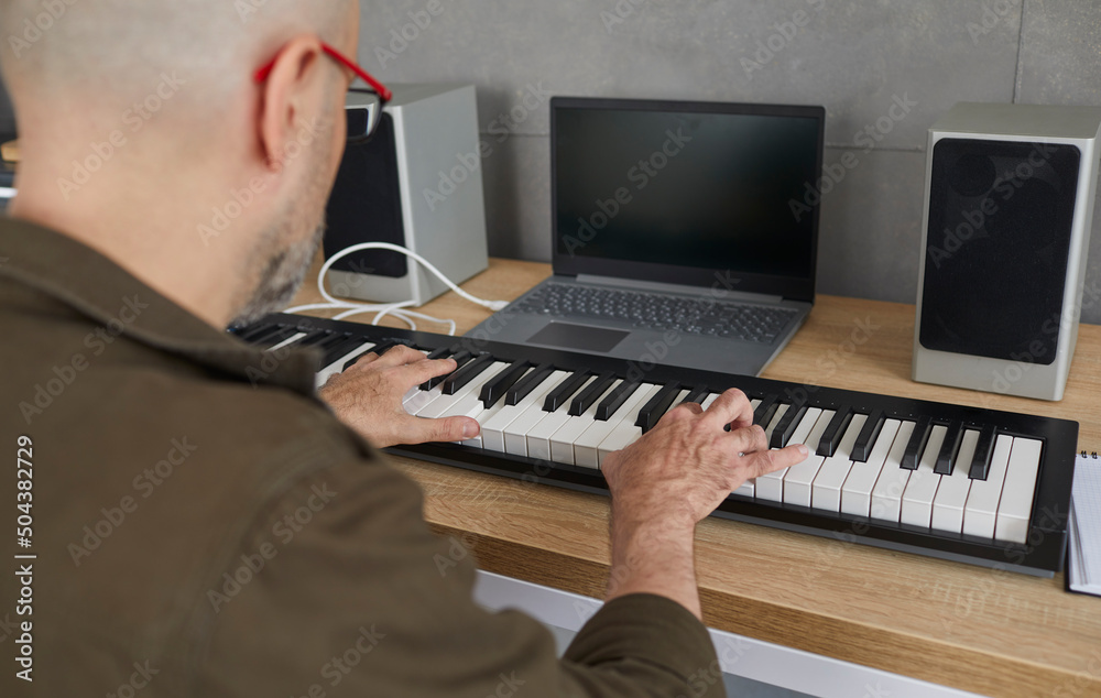 Man is rehearsing while playing on compact modern synthesizer in his home music studio. Close up of hands of bald middle-aged man who presses synthesizer keys while creating new music. Selective focus Man is rehearsing while playing on compact modern synthesizer in his home music studio. Close up of hands of bald middle-aged man who presses synthesizer keys while creating new music. Selective focus