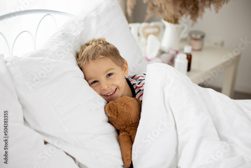 Sweet blond preschool child with teddy bear, lying in bed sick,