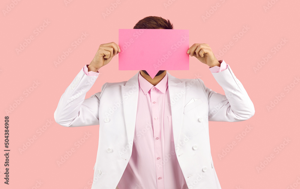Anonymous man in suit hiding his face behind blank rectangular message bubble. Unrecognizable guy holding speech balloon, voicing out his thought, sharing his opinion. Studio shot on pink background Anonymous man in suit hiding his face behind blank rectangular message bubble. Unrecognizable guy holding speech balloon, voicing out his thought, sharing his opinion. Studio shot on pink background
