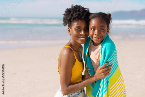 Portrait of smiling african american young mother wrapping daughter with towel against sea and sky © WavebreakMediaMicro