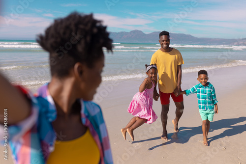 African american young woman looking at happy son, daughter and boyfriend at beach against sky © WavebreakMediaMicro
