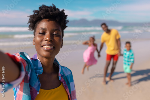 Portrait of smiling african american young woman with son, daughter and man in background at beach © wavebreak3