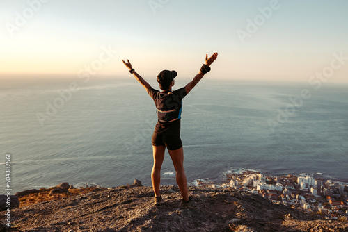 Rear view of fit woman standing on mountain top looking at view with arms wide open