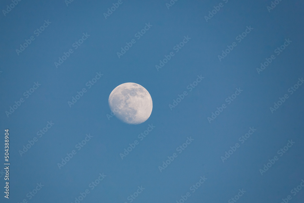 Close up of new moon with visible craters on its surface on blue day sky background with copy space Close up of new moon with visible craters on its surface on blue day sky background with copy space