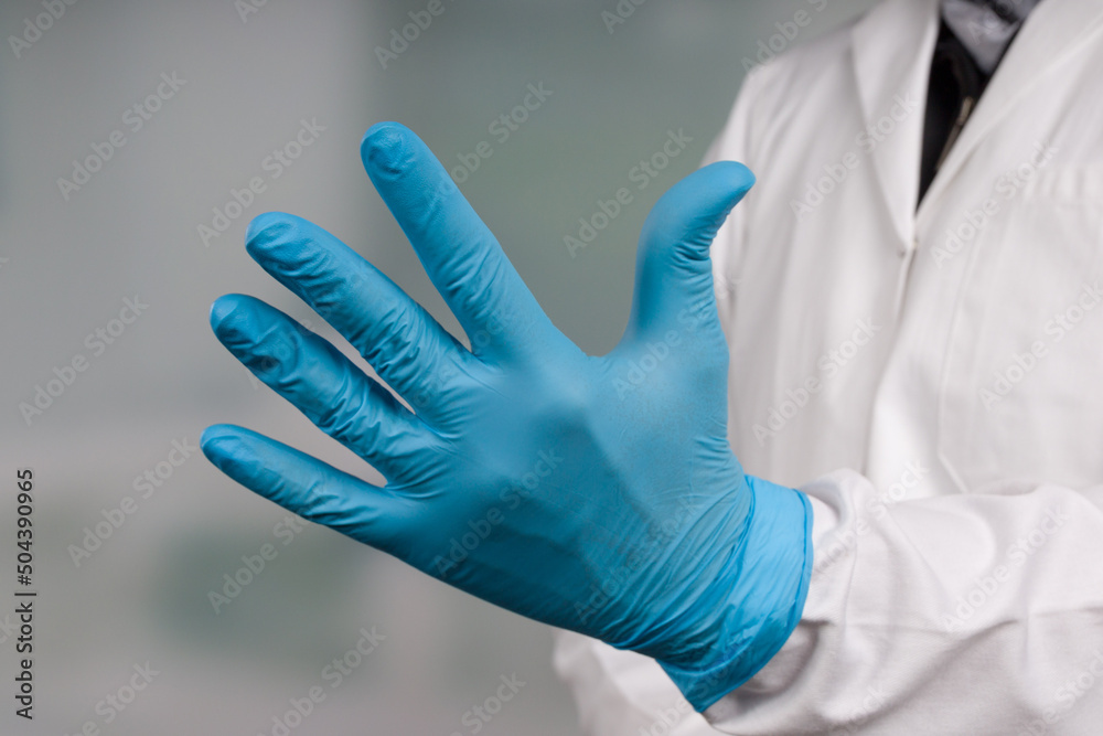 Close-up of hands putting on medical gloves in front of a clinic/ICU room Close-up of hands putting on medical gloves in front of a clinic/ICU room