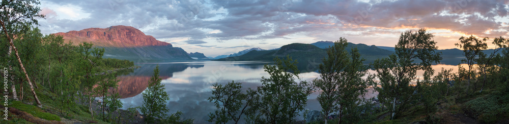 Panoramic view of beautiful blue pink sunrise over the lake dam on river Lulealven in Saltoluokta in Sweden Lapland. Reflection of pink mountains and sky with dramatic clouds in clear calm water.
