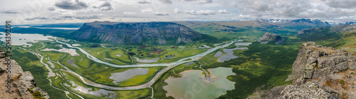 Aerial panoramic scenic view from Skierffe rock summit on glacial Rapadalen river delta valley at Sarek national park with meanders, lakes, mountains, birch trees. Summer day landscape Sweden Lapland