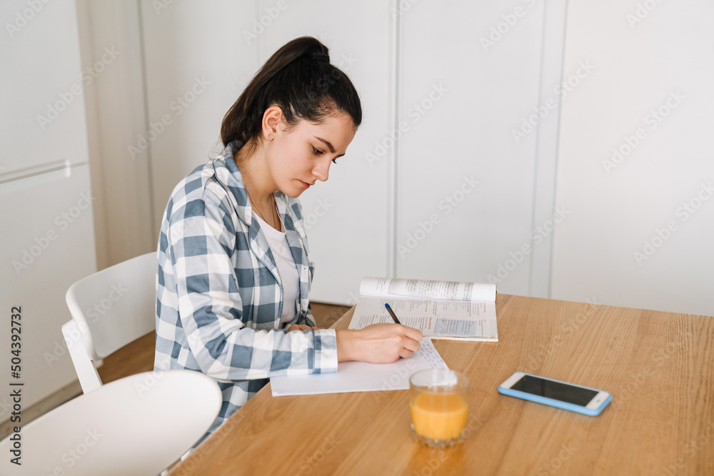 Young woman doing homework while sitting at table in kitchen Young woman doing homework while sitting at table in kitchen