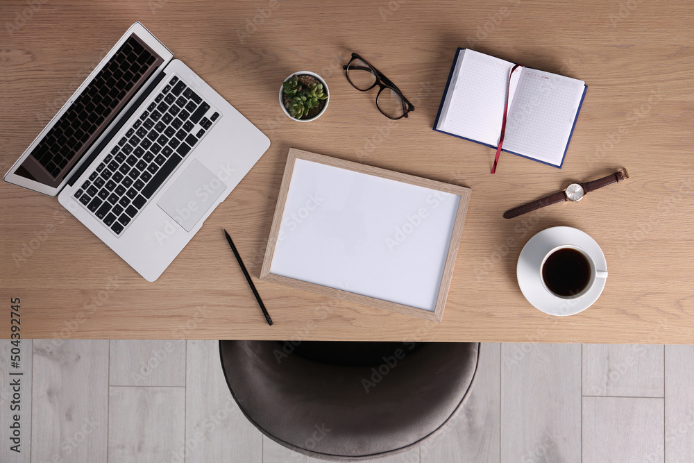 © New Africa - Chair near wooden table with laptop, cup of coffee and stationery indoors, top view