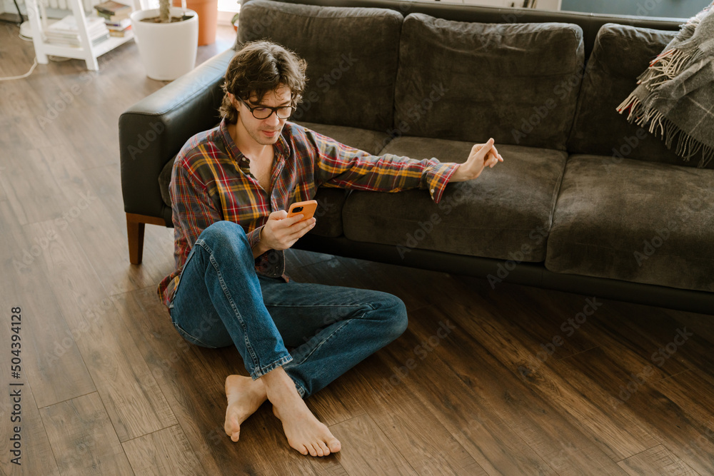 White man in glasses using mobile phone while sitting on floor