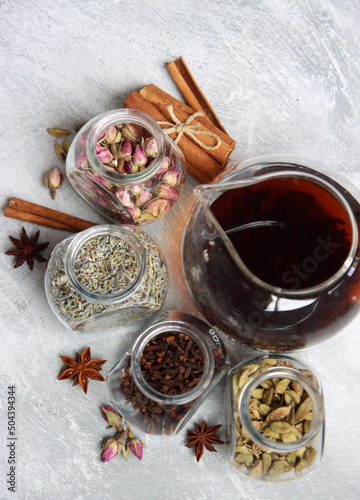 Teapot and spices jars on light grey background with copy space. Different tea flavors on a table. Lavender, cardamom, cinnamon, rose, anise stars and clove top view photo. 