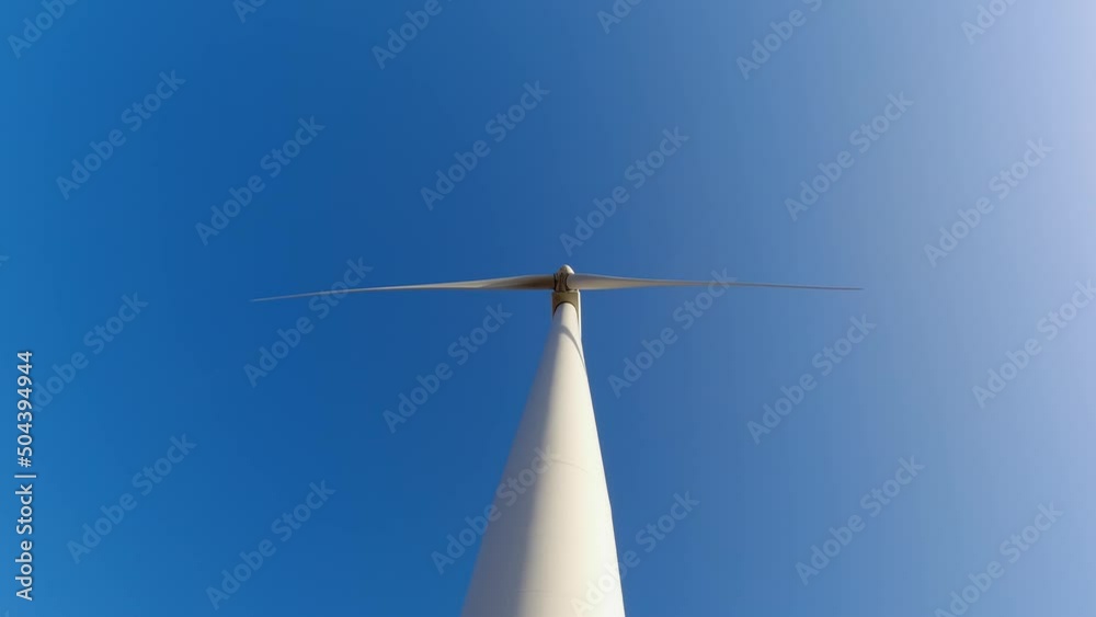 Large wind turbine with blades in the field below view. Blue sky panorama. Windmills farm generating green energy. Sustainable alternative energy. Slow movement. Large wind turbine with blades in the field below view. Blue sky panorama. Windmills farm generating green energy. Sustainable alternative energy. Slow movement.