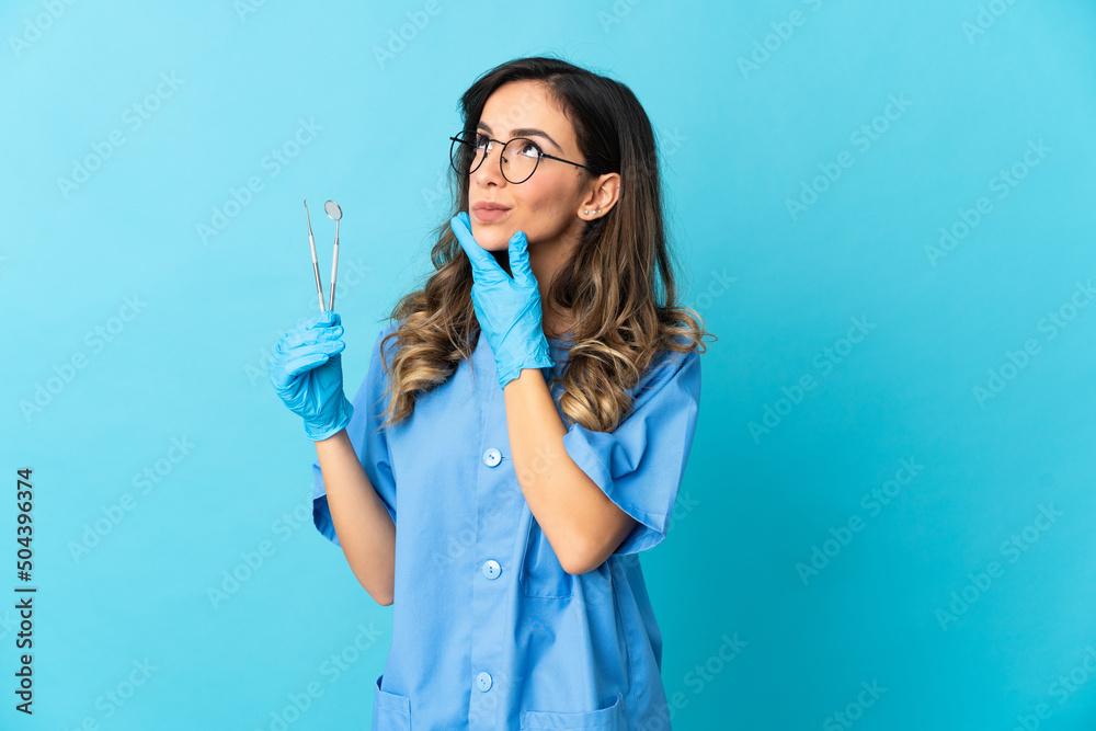 Woman dentist holding tools over isolated on blue background looking up while smiling Woman dentist holding tools over isolated on blue background looking up while smiling