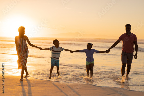 African american young parents holding son and daughter's hands while standing at shore against sky