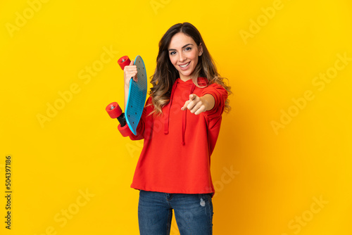 Young caucasian woman isolated on yellow background with a skate and pointing to the front