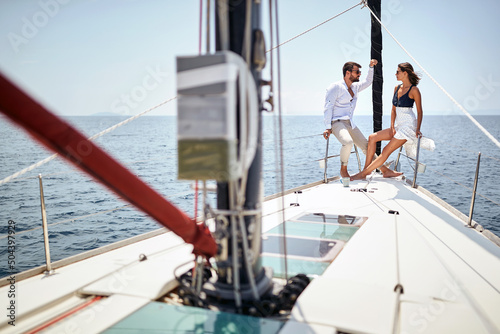 A young couple is chatting and posing for a photo on the bow of the yacht while enjoying a ride on the sea. Summer, sea, vacation, relationship
