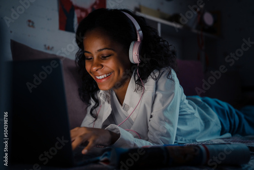 Young african girl in headphones liying in front of laptop photo